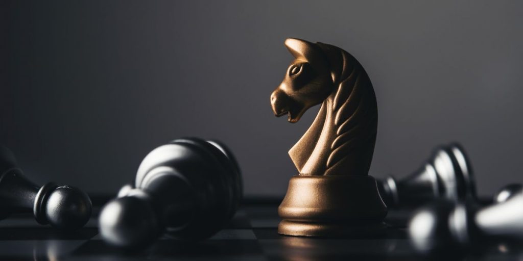 Knight chess piece standing among toppled pawns.